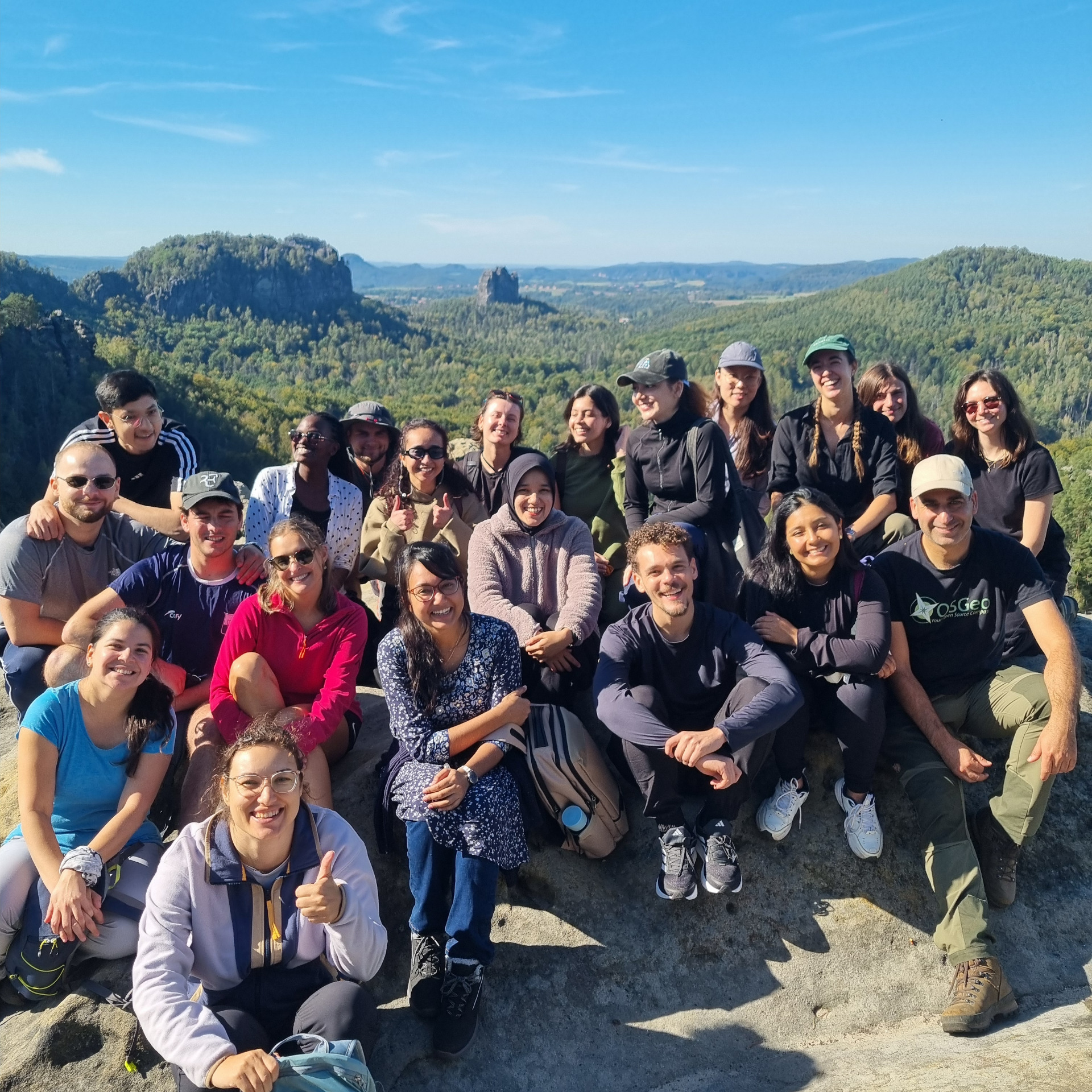 Group picture on a cliff overlooking green valleys and distant rock formations.