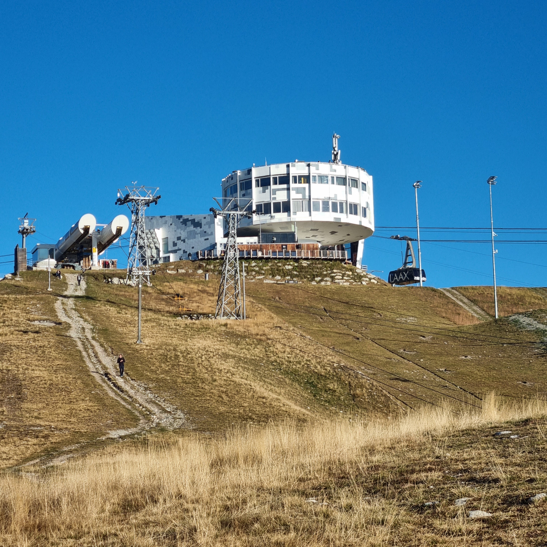 Large white building on a hillside with antennas and satellite dishes against a clear blue sky.